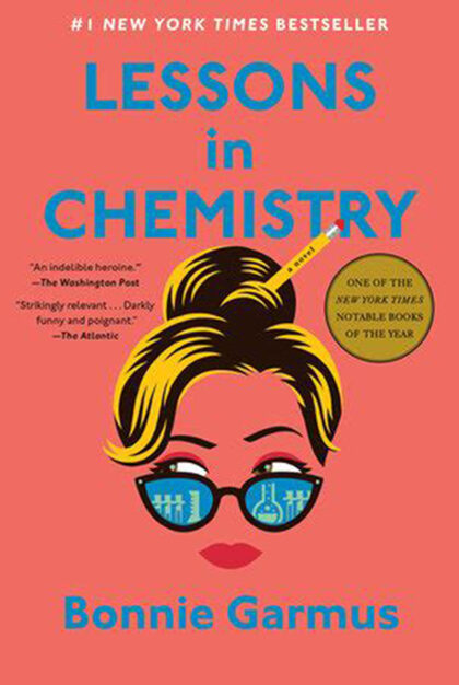 A salmon-colored cover of Bonni Garmus' book Lessons in Chemistry with a female face wearing glasses with dirty blonde hair in a bun with a pencil through it.